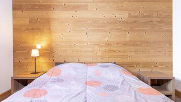 Ein Schlafzimmer mit einem Holz-Kopfteil, einem Bett mit einem gemusterten Überwurf, einem Nachttisch mit einer Lampe und einem zusätzlichen Nachtschränkchen.