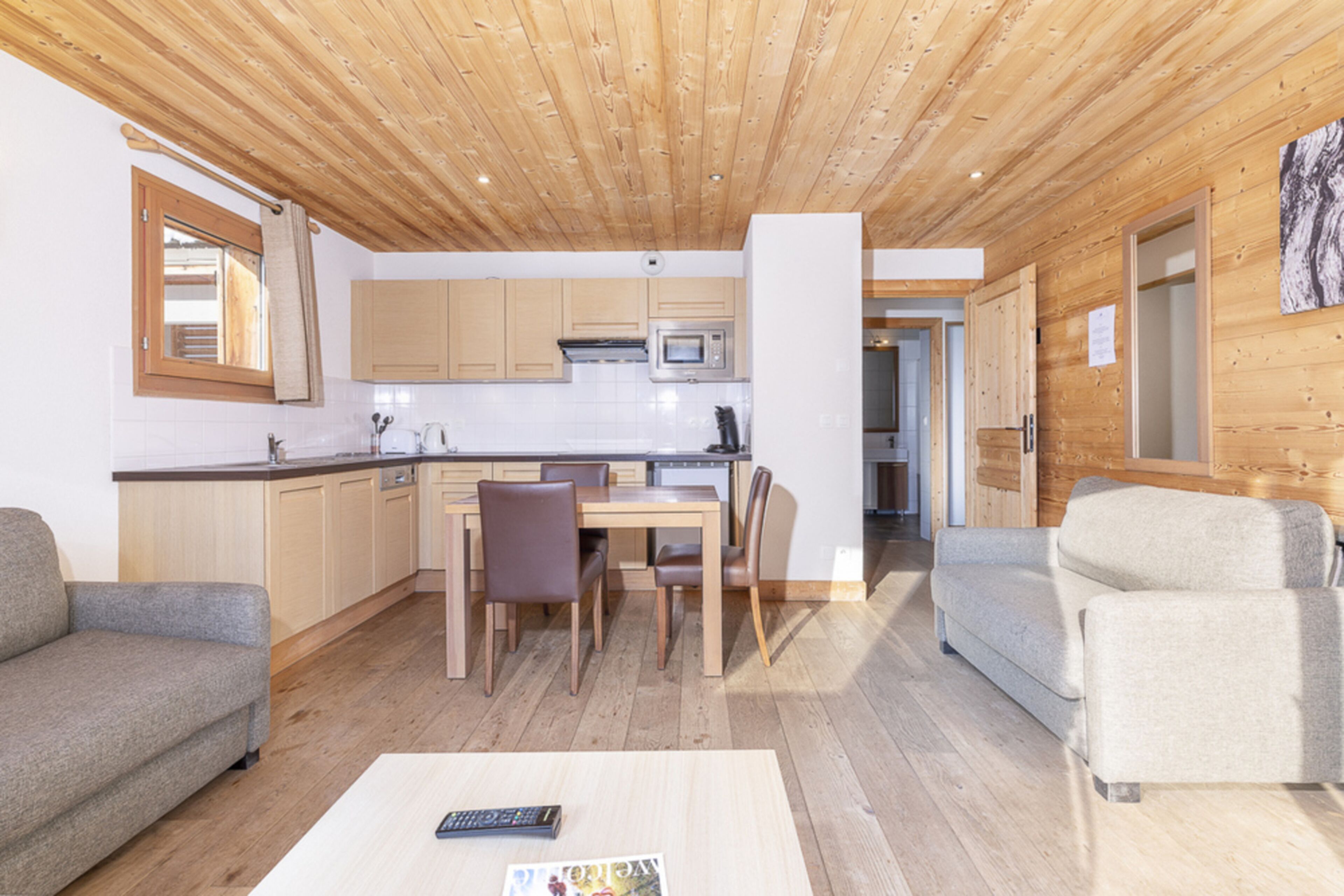 Un interior moderno con techo de madera, una zona de cocina con microondas, una mesa de comedor con sillas y dos sofás.