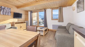 A cozy cabin interior with a wooden dining table, sofa, and a TV mounted on the wall.