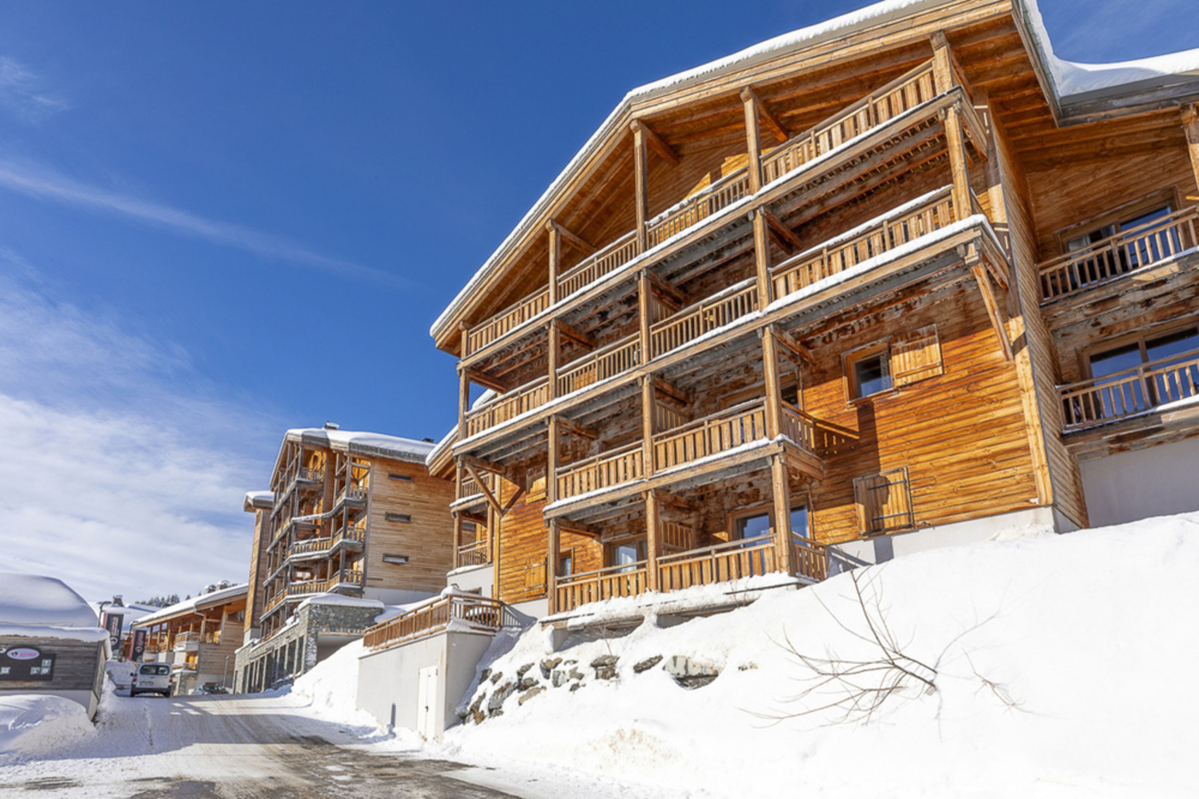 A multi-story wooden building with balconies, a snow-covered ground, and a clear blue sky.