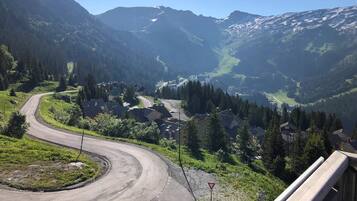 Une route sinueuse qui traverse une région montagneuse, bordée de maisons et de verdure.
