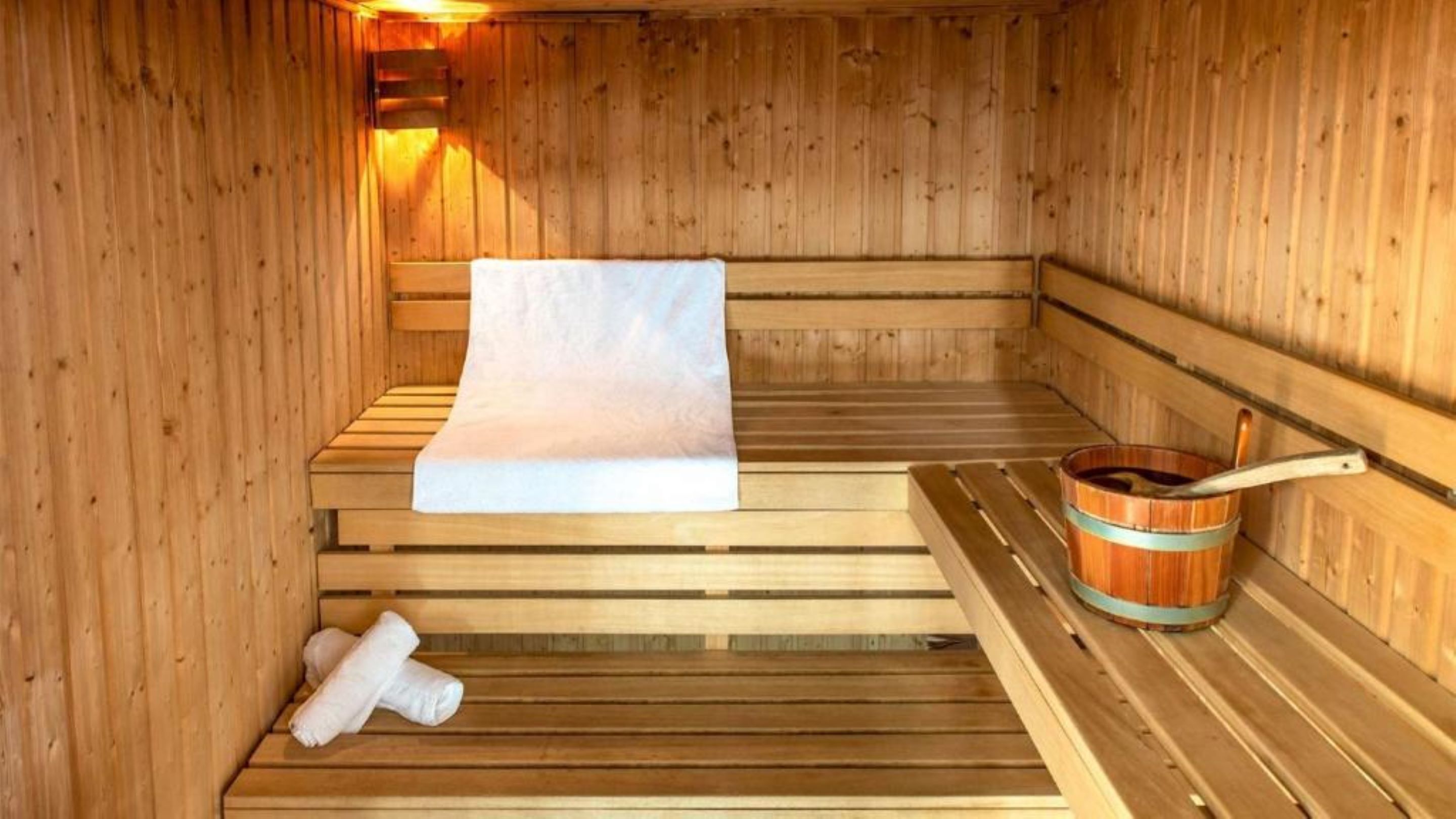 Un sauna en bois avec des bancs, un banc avec une serviette et un seau en bois avec une louche.