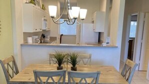 Un coin repas avec une table et des chaises en bois, un lustre et une cuisine en arrière-plan.
