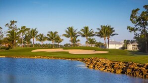 Un parcours de golf avec un plan d’eau, des palmiers et un bâtiment en arrière-plan.