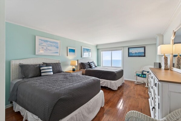 A bedroom with two beds, a dresser, and a view of the ocean.