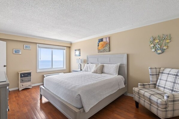 A bedroom with a large bed, a chair, a nightstand, a window with a view, and wall art.