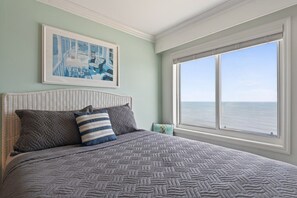 A bedroom with a large window, a bed with patterned bedding, and a framed picture on the wall.