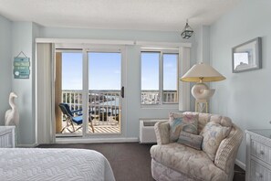 Ein Zimmer mit Bett, Sessel, Sofa, Lampe und Blick auf einen Balkon mit Geländer.