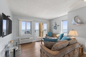 A living room with a sofa, a television, and a view of the ocean through large windows.
