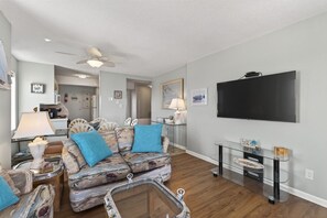 Un salon avec un canapé, une table basse, un téléviseur et un ventilateur de plafond.