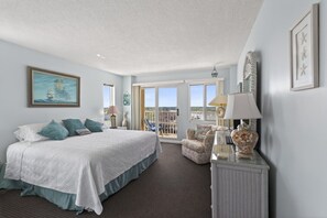 A hotel room with a bed, a chair, a table, and a balcony with a view.