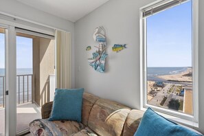 A balcony with a view of the beach, a sofa with cushions, and wall art. - Corner Unit w/Sunrise & Sunset Views!| Pool | 1307 (Virginia Beach)