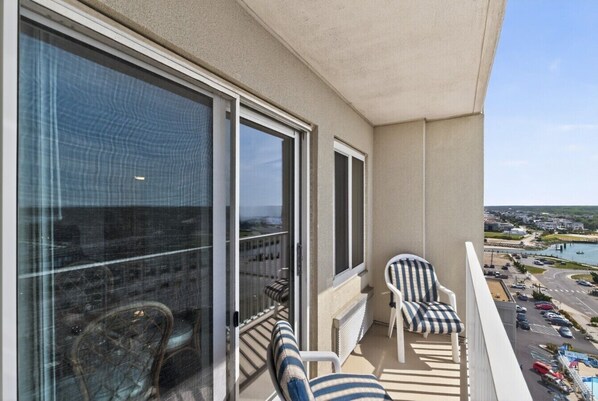 A balcony with two chairs, a view of the sea, and a parking area.