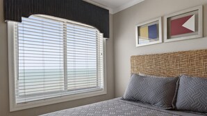 A bedroom with a large window, a bed with patterned bedding, a woven headboard, and two framed artworks on the wall.