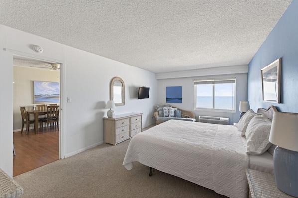 A bedroom with a large bed, a dresser, a chair, a TV, and a window with a view.