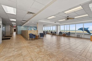 A spacious lobby with a reception desk, seating area, and large windows offering a view of the beach. - Wake Up to Ocean Views |Relax & Watch the Waves! (Virginia Beach)