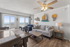 Un salon spacieux doté d’un plancher en bois, d’un ventilateur de plafond, d’un canapé, d’une table basse et d’un coin repas avec des chaises et une table.