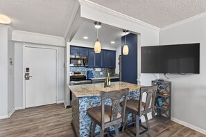 A modern kitchen with granite countertops, dark blue cabinets, and a large island with bar stools. - Beachwalk Modern Condo Overlooking Ocean Sunshine! (Virginia Beach)