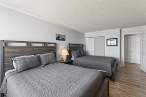 Une chambre d’hôtel avec deux lits, une table de chevet avec une lampe, un tableau au mur et un ensemble de portes blanches.