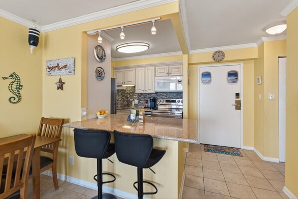 A kitchen with a bar area, a dining table with chairs, and a microwave. - Ocean Front Balcony on the Beach | Watch Dolphins! 704 (Virginia Beach)