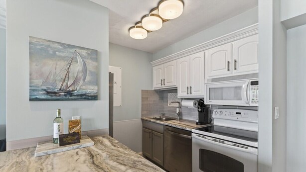 A kitchen with white cabinets, a marble countertop, a stainless steel oven, a microwave, and a coffee maker.