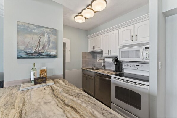 A kitchen with white cabinets, a marble countertop, a stainless steel oven, a microwave, and a coffee maker.
