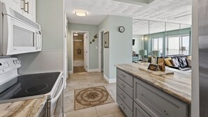 A kitchen with white cabinets, a stove, and a microwave. There is a hallway leading to a bathroom.
