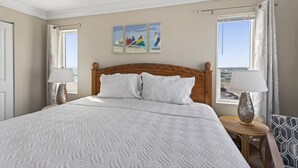 A hotel room with a large bed, two bedside lamps, a view of the city, and a painting on the wall.