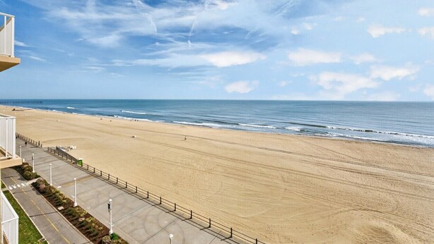 A beach with a clear sky, a sandy shore, and a building with a balcony overlooking the beach.