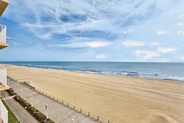 Una playa con cielo despejado, una orilla arenosa y un edificio con balcón que da al mar.