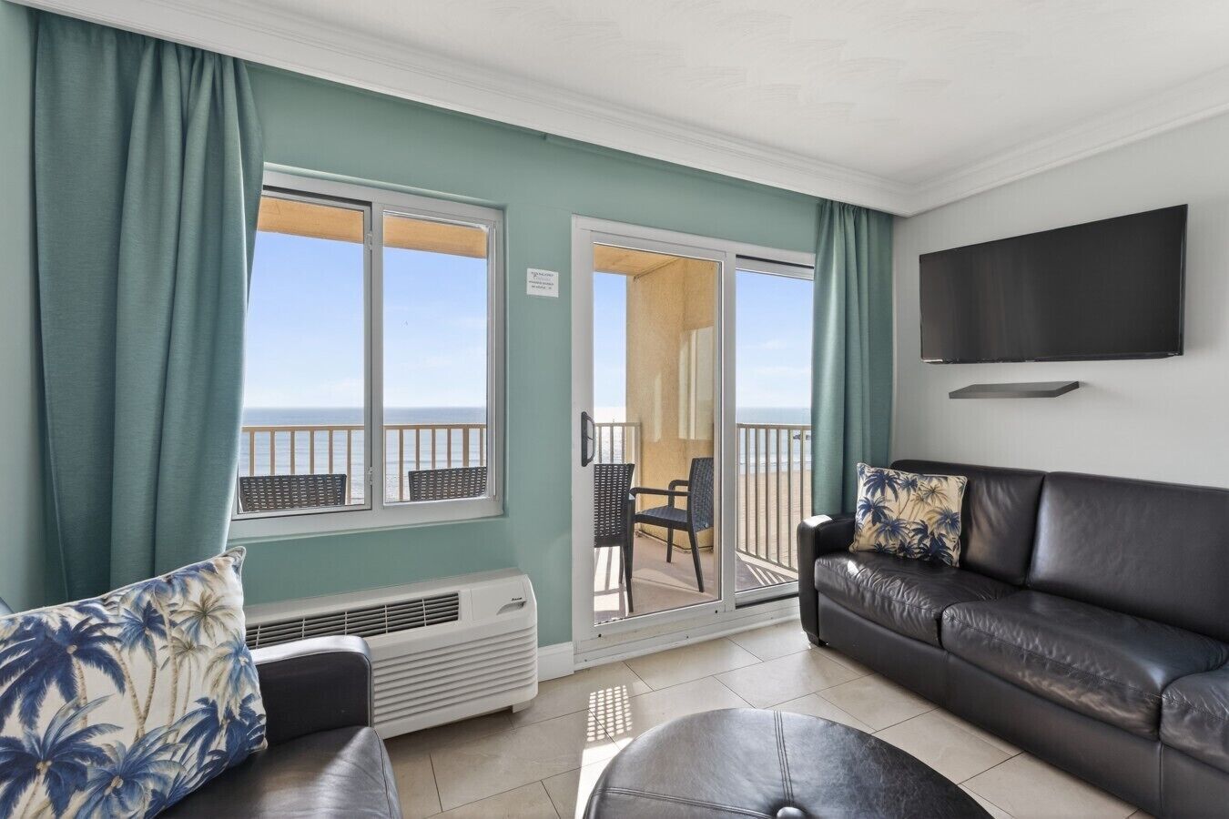 A living room with a sofa, a chair, a television, and a view of the ocean through large windows.