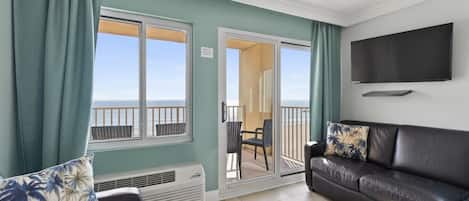 A living room with a sofa, a chair, a television, and a view of the ocean through large windows.