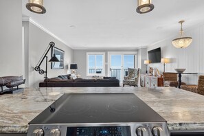 A modern kitchen with a built-in stovetop, a dining area with a round table, and a seating area with a sofa and chairs.