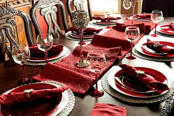 Una mesa formal para comedor cubierta con manteles rojos, platos blancos y servilletas rojas.
