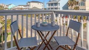 A balcony with two chairs and a small table, overlooking a street with houses and a clear sky. - Beach Nest 2 Stylish Condo  2 Min Walk to Beach (North Myrtle Beach)