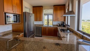 Une cuisine moderne dotée de plans de travail en granit, d’appareils électroménagers en acier inoxydable, d’armoires en bois et d’une grande fenêtre offrant une vue dégagée.