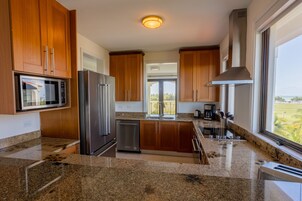 Una cocina moderna con encimeras de granito, electrodomésticos de acero inoxidable, armarios de madera y un amplio ventanal con vistas.