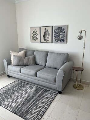 A modern living room with a grey sofa, a patterned rug, and three framed botanical prints on the wall. - The Country Club Residences at Grand Reserve (Río Grande)