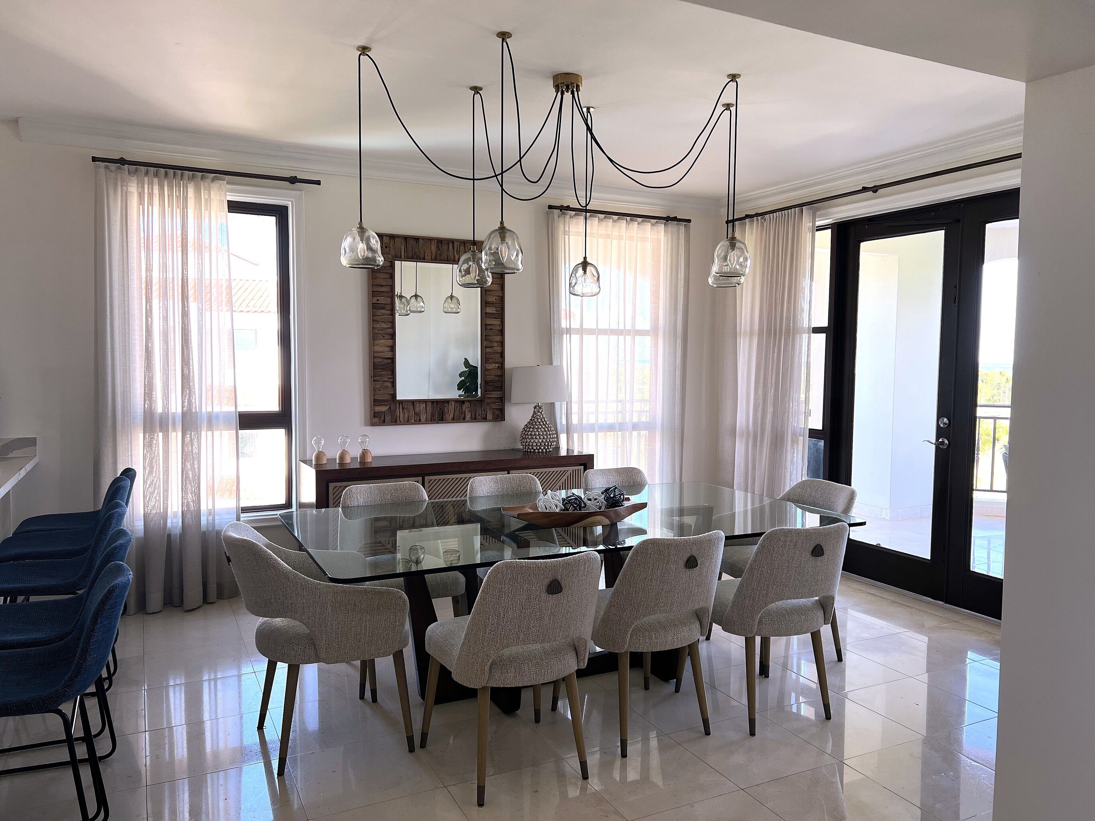A dining area with a glass table, six chairs, a wooden bench, and a chandelier.