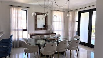 A dining area with a glass table, six chairs, a wooden bench, and a chandelier.