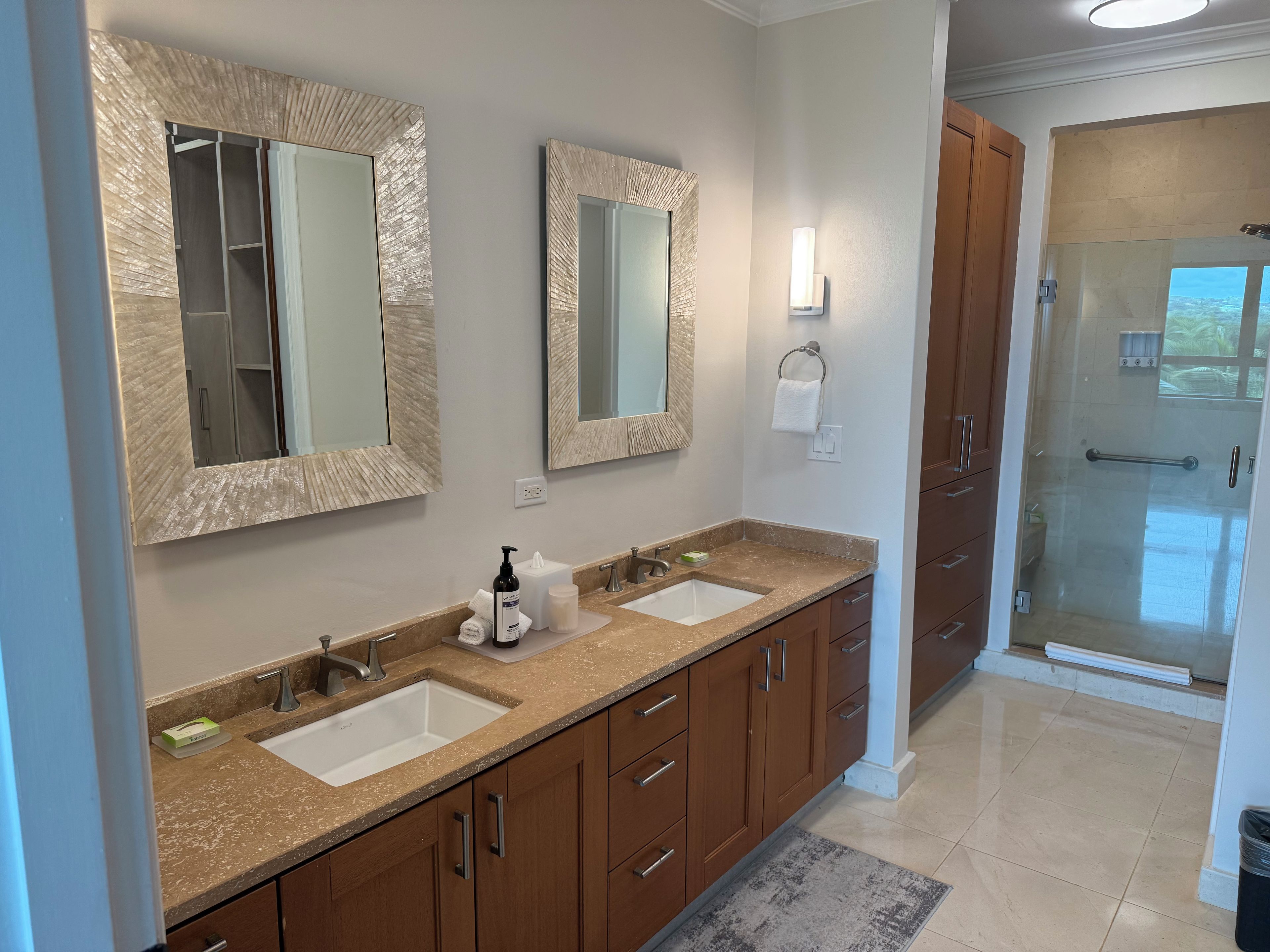 A bathroom with two sinks, wooden cabinets, a glass shower enclosure, and a towel rack.