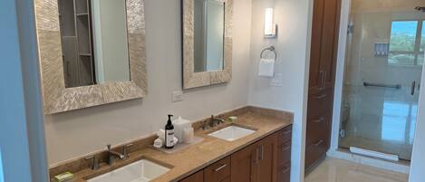A bathroom with two sinks, wooden cabinets, a glass shower enclosure, and a towel rack.