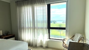 Ein Schlafzimmer mit zwei Betten, einem Fenster mit Meerblick und einem Sessel mit Decke.