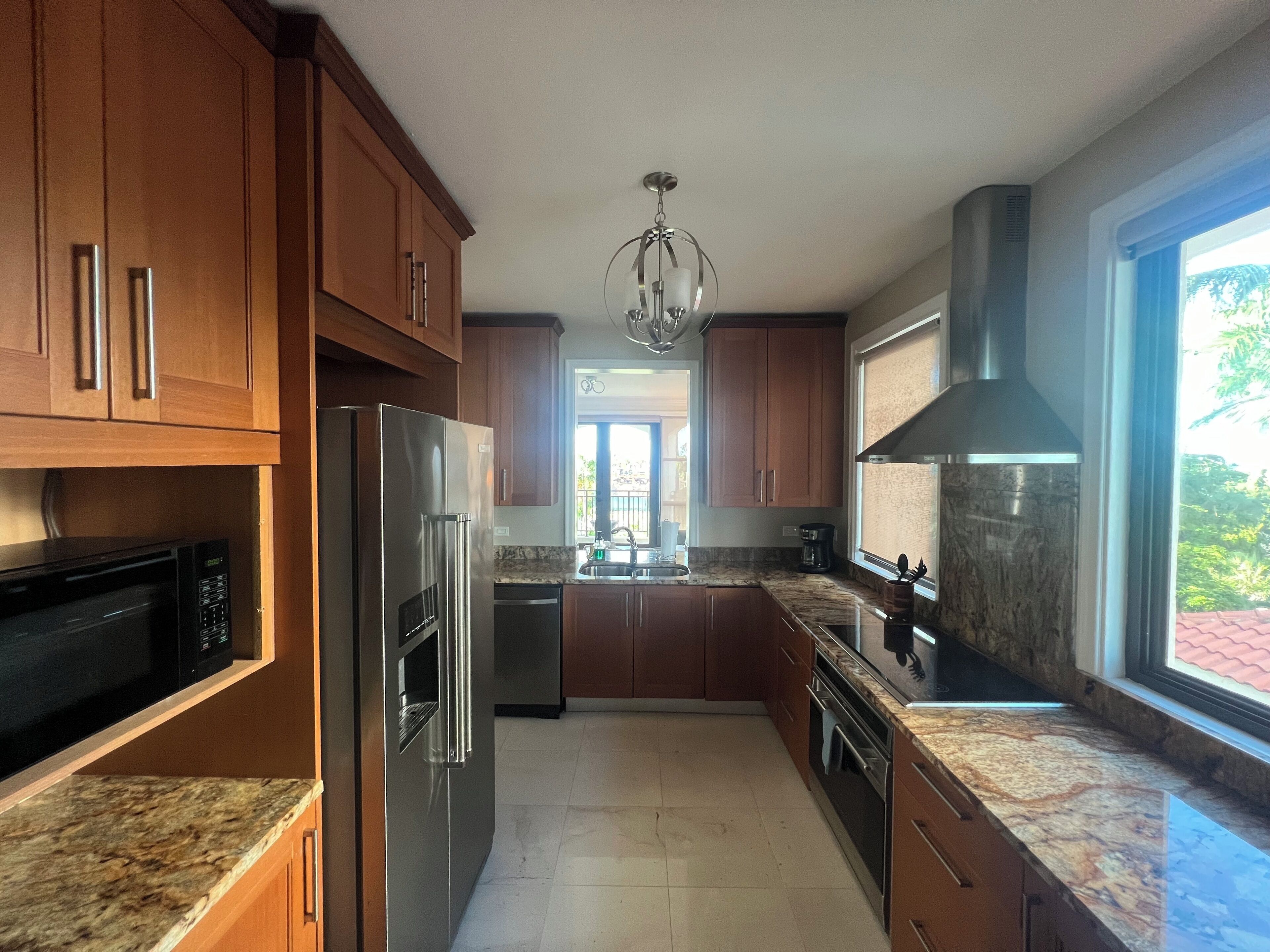 A modern kitchen with wooden cabinets, stainless steel appliances, granite countertops, and a large window offering a view of greenery.