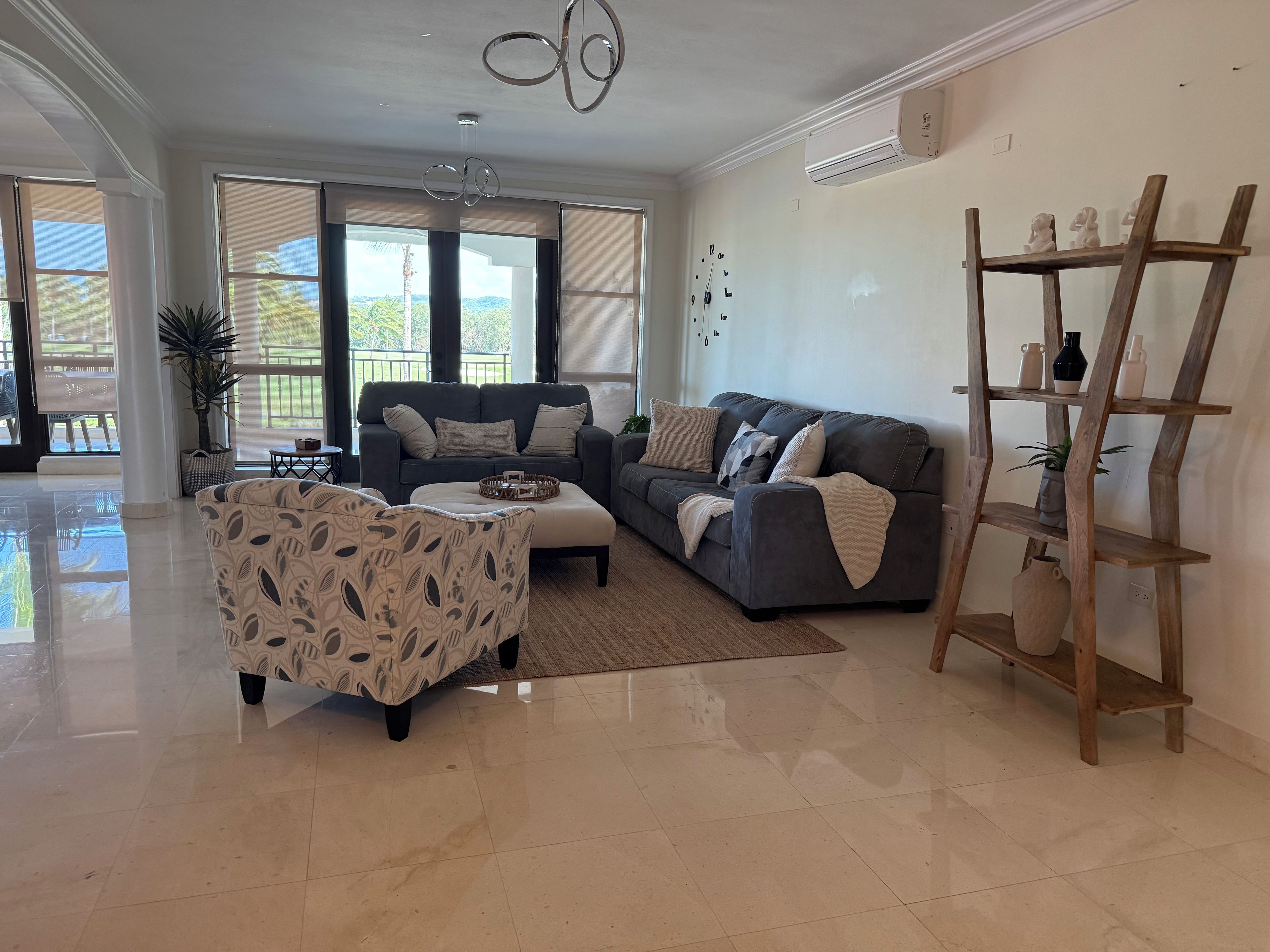 Amplia sala de estar con un sofá gris, un sillón estampado y un estante de madera con objetos decorativos.