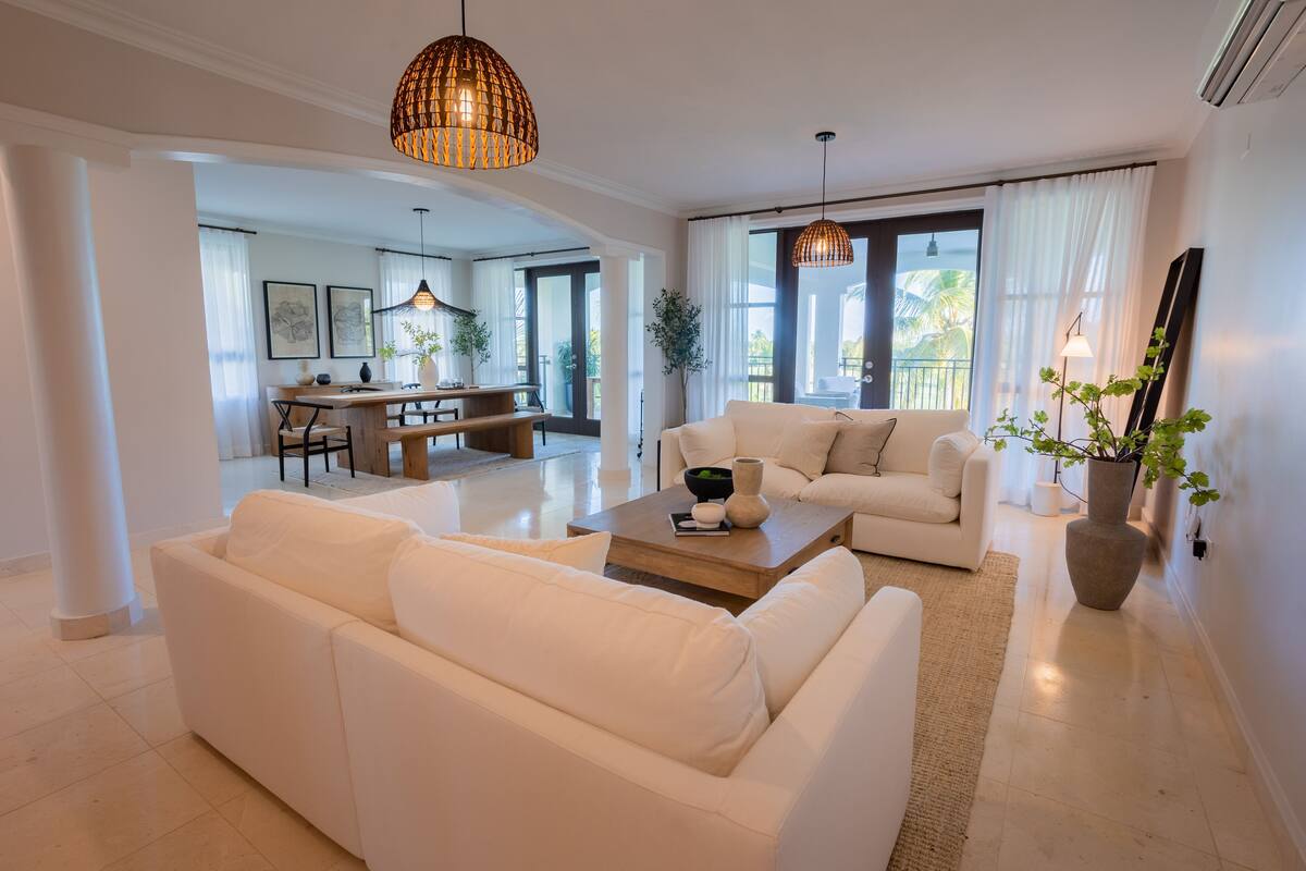 Ein geräumiges Wohnzimmer mit einem weißen Sofa, einem Holztisch und einem Essbereich im Hintergrund.