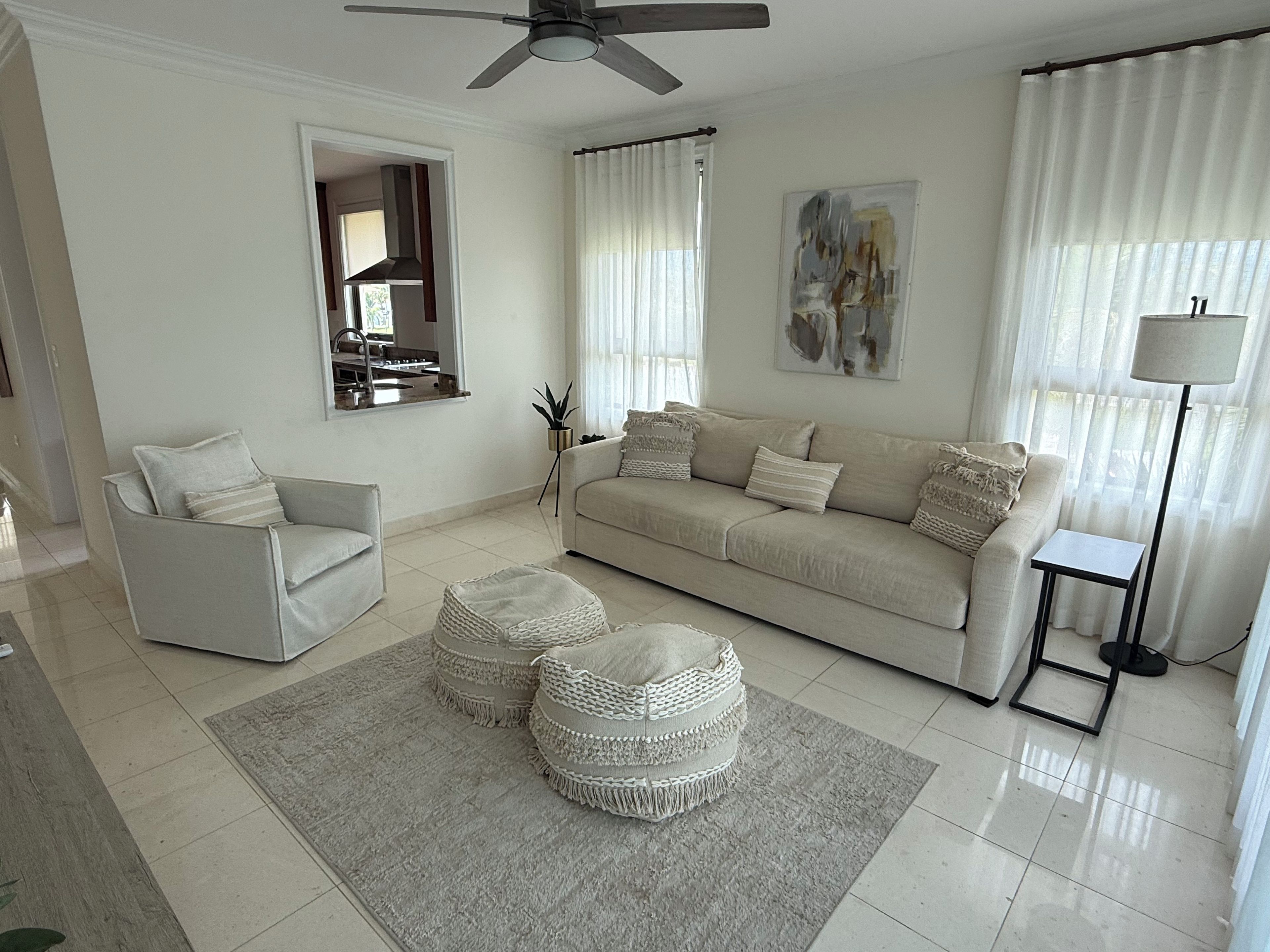 Una sala moderna con sofá, sillón, pufs y una lámpara de pie.
