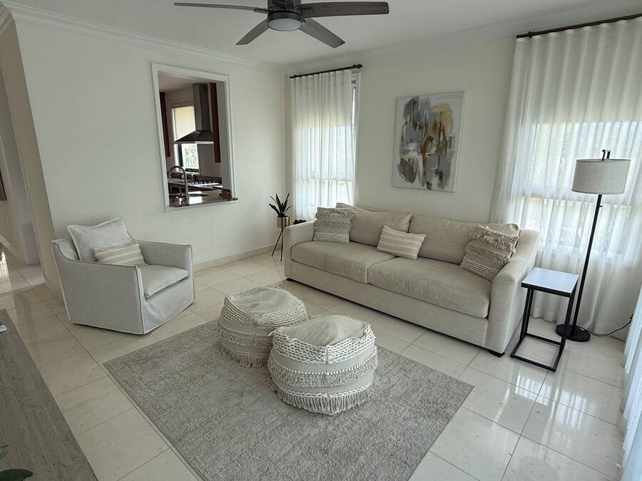 Una sala moderna con sofá, sillón, pufs y una lámpara de pie.