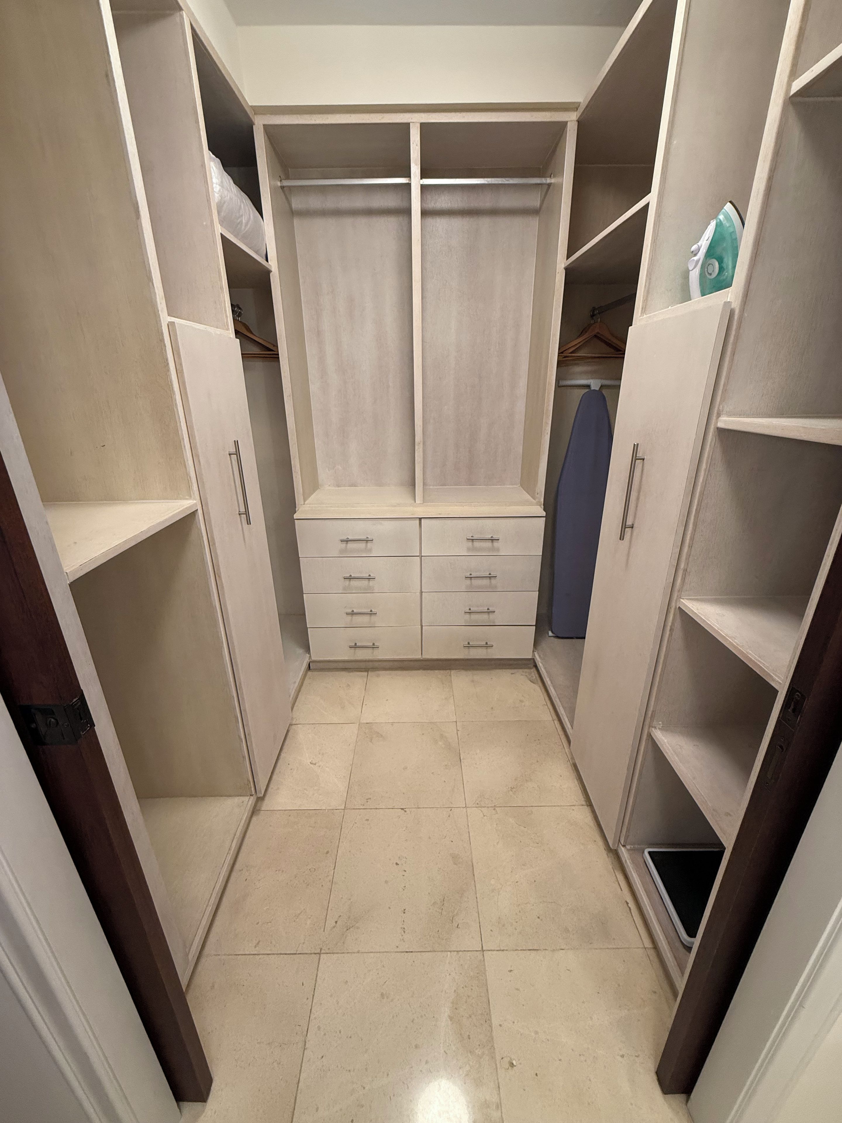 A walk-in closet with open shelves, a central drawer unit, and a hanging space.