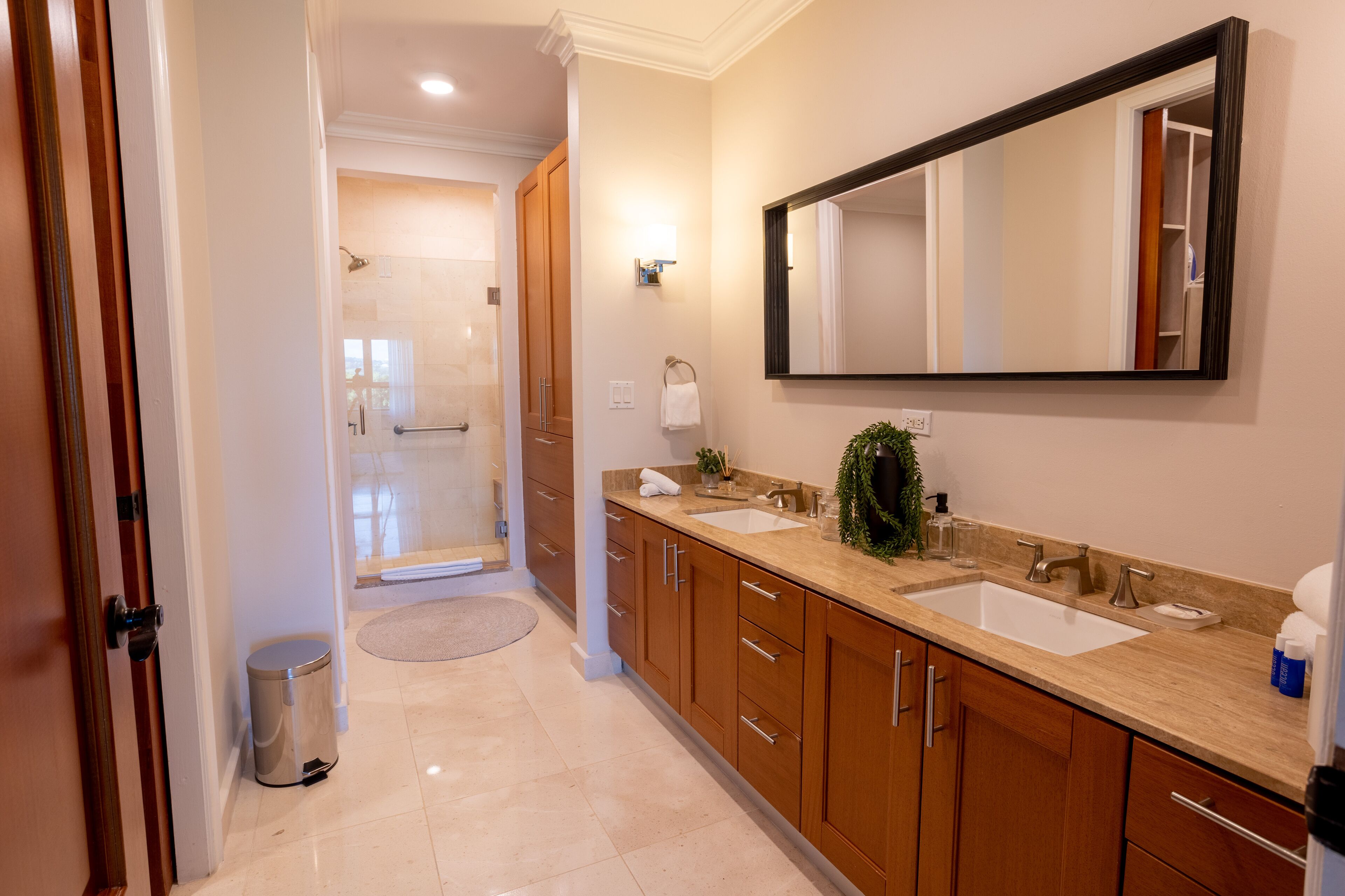 A modern bathroom with two sinks, wooden cabinets, a large mirror, and a shower area.